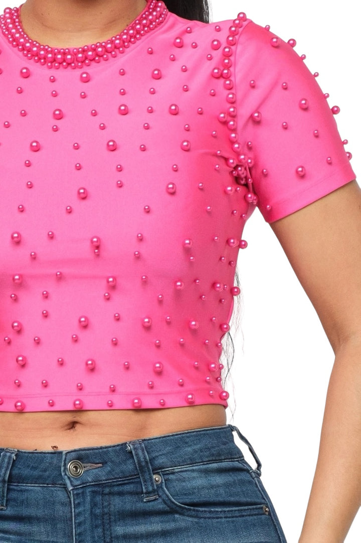 a woman wearing a pink top with pearls on it