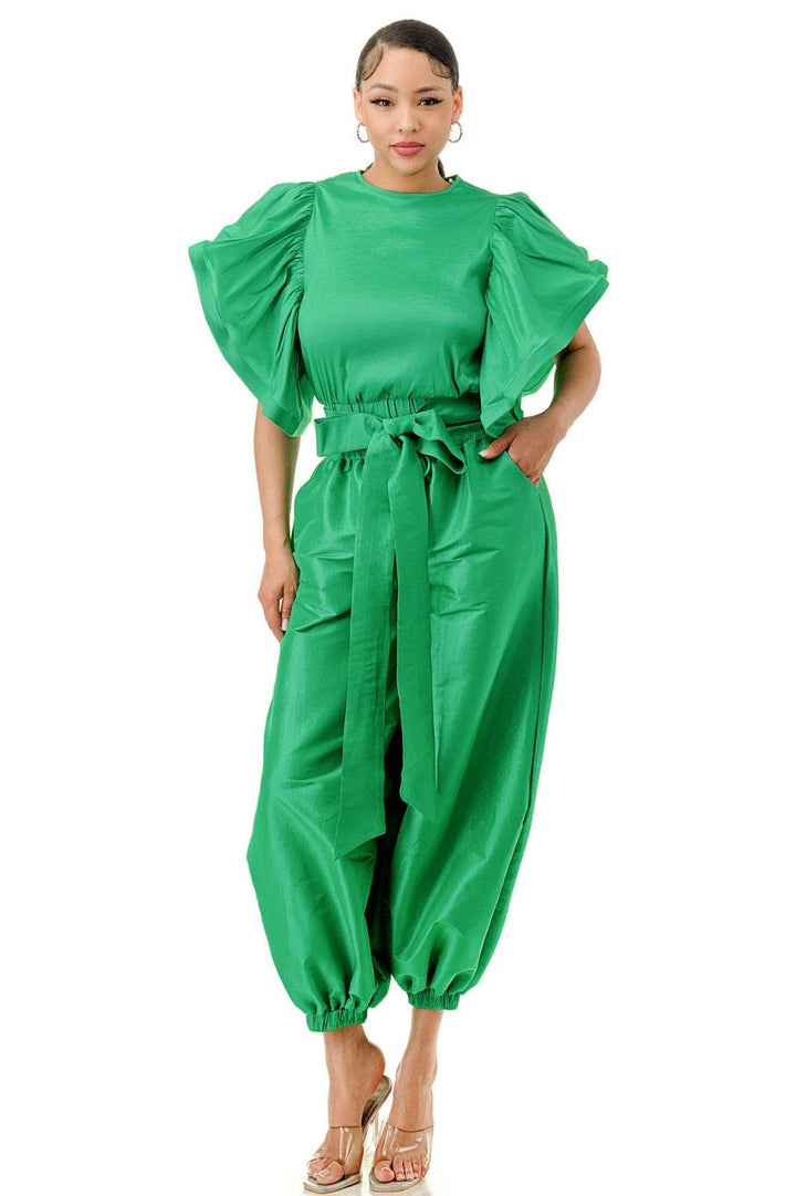 a woman wearing a green jumpsuit and sandals